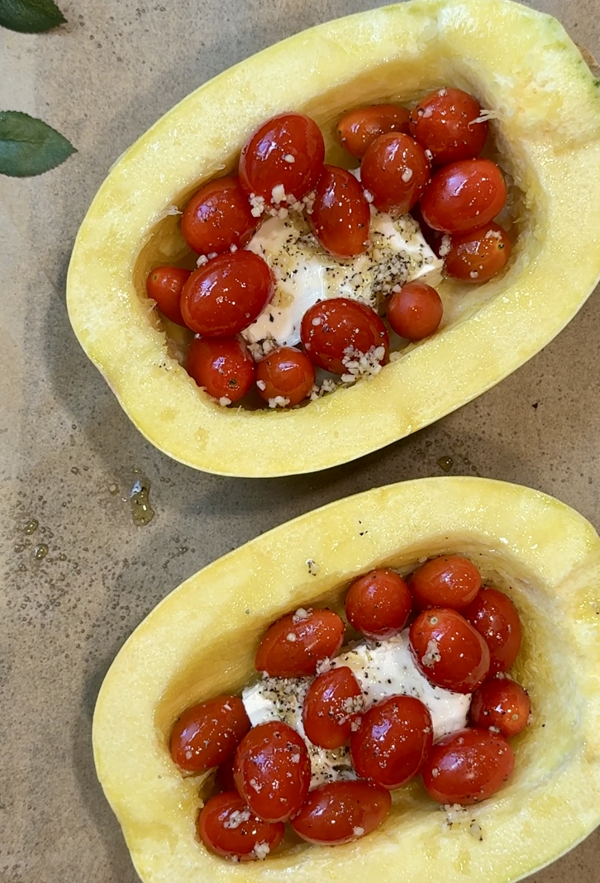 Two halves of spaghetti squash filled with cherry tomatoes, crumbled cheese, minced garlic, pepper, and olive oil—this baked feta spaghetti squash makes a perfect low-carb dinner, all set on a baking sheet and ready for the oven.