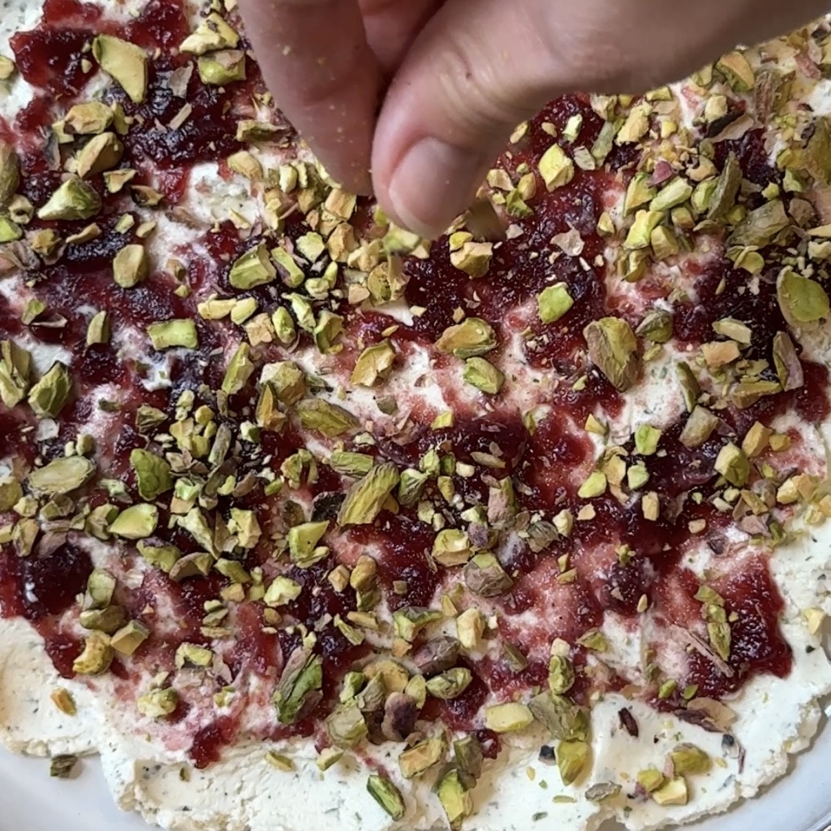 A serving platter with Boursin cheese, jam and pistachios.