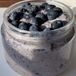 A glass jar with blended blueberry overnight oats, topped with more fresh blueberries