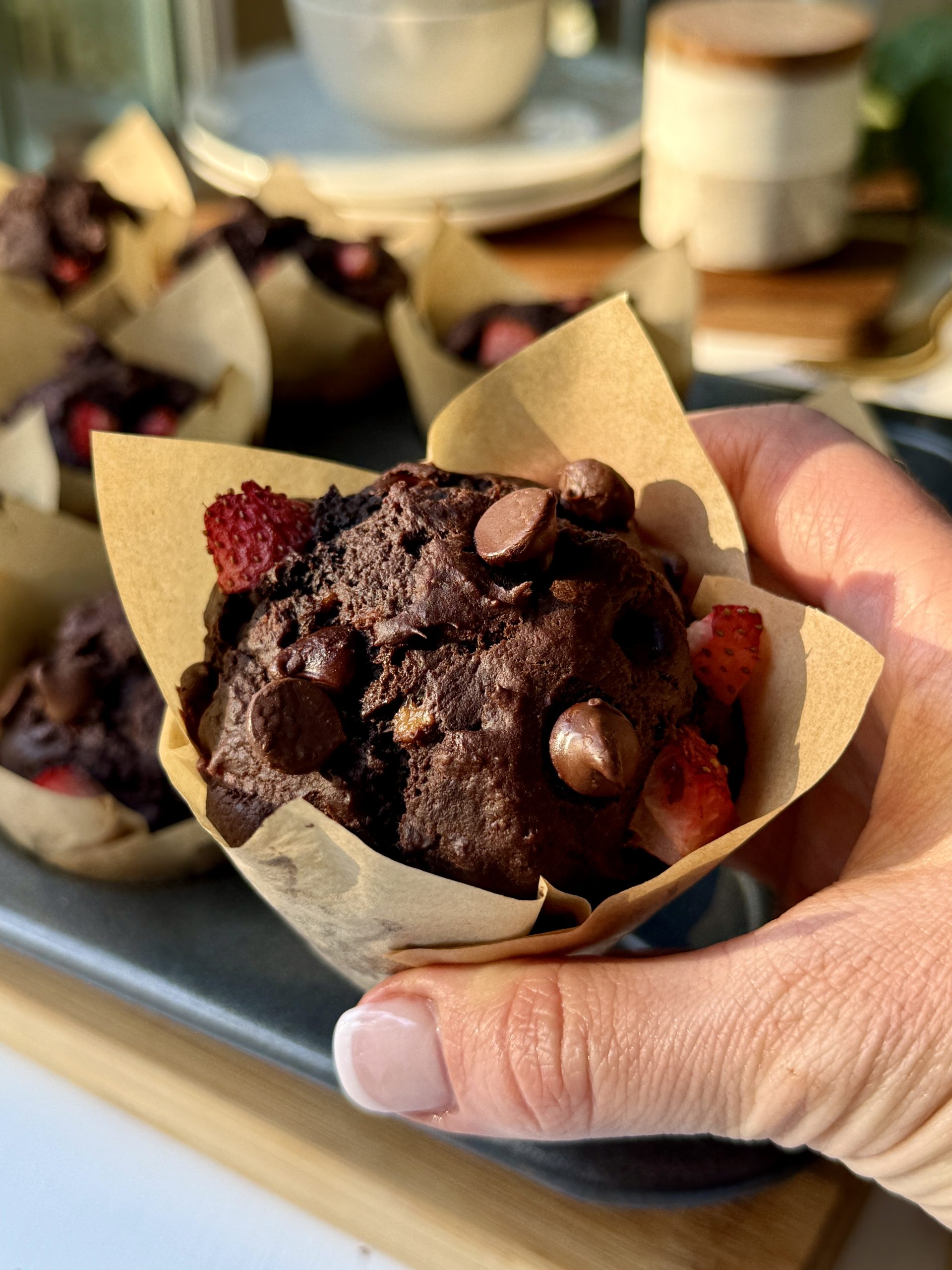 A picture of a hand holding a chocolate muffin with strawberries and chocolate chips. It's