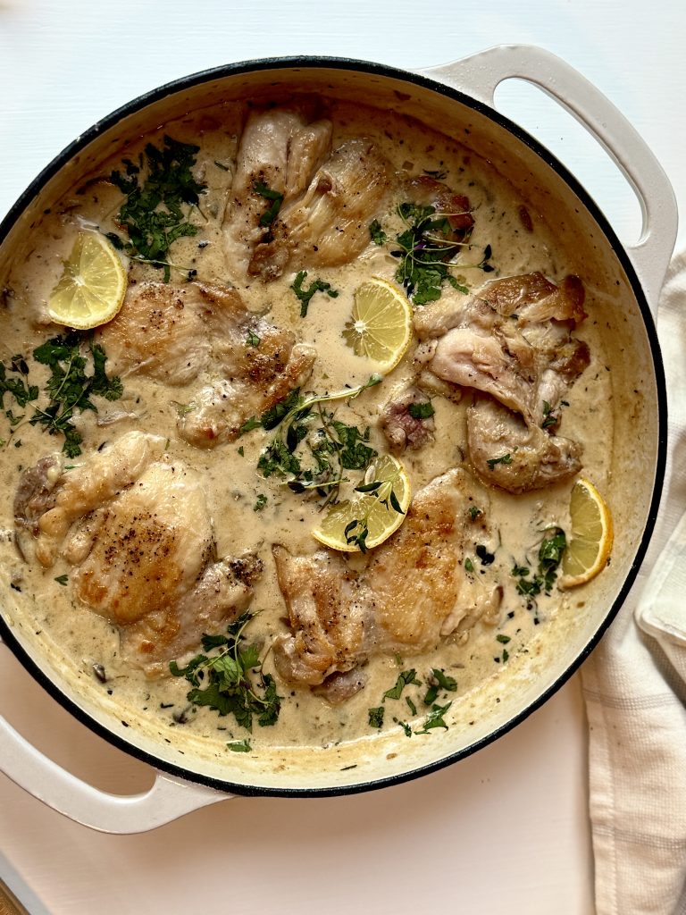 Creamy lemon chicken in a beige skillet, garnished with fresh herbs and lemon slices. The dish exudes a warm, savory, and inviting tone.