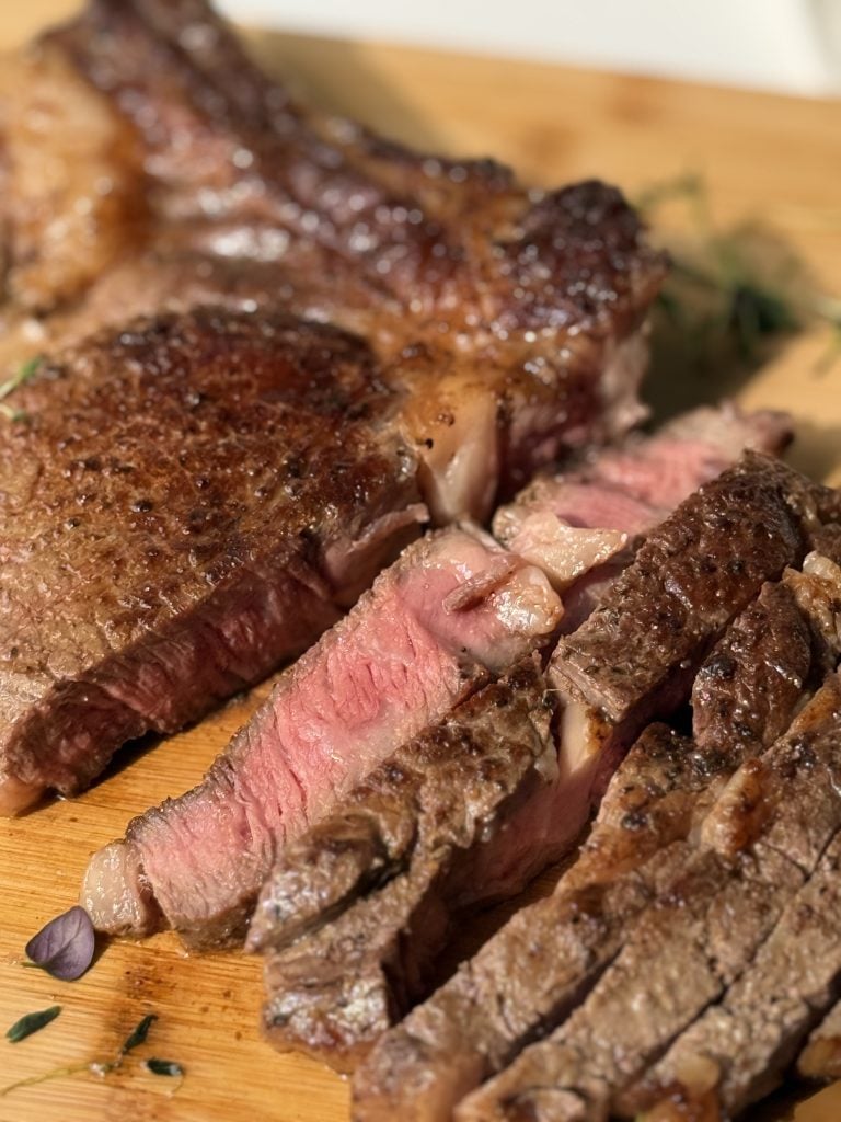 Close-up of a perfectly seared steak on a wooden board, sliced to reveal juicy pink meat with a crispy brown crust, evoking a savory, satisfying meal.
