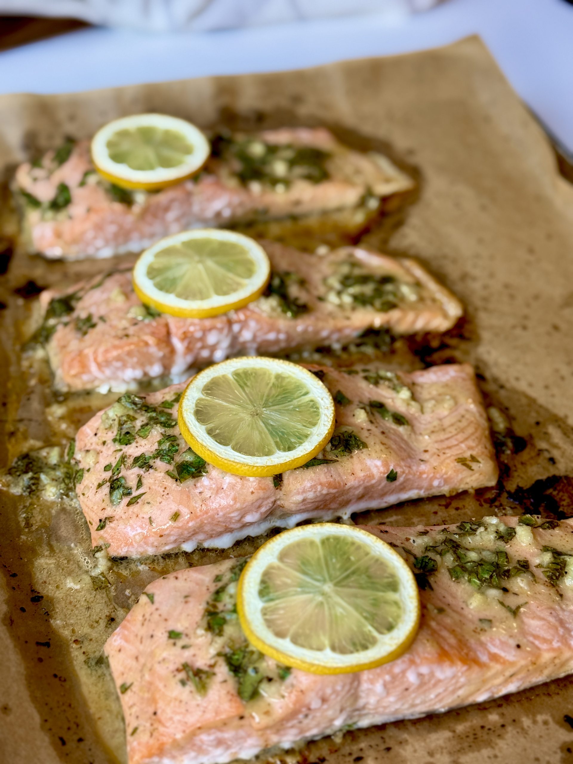 Baked salmon fillets on parchment paper, topped with garlic herb butter and lemon slices
