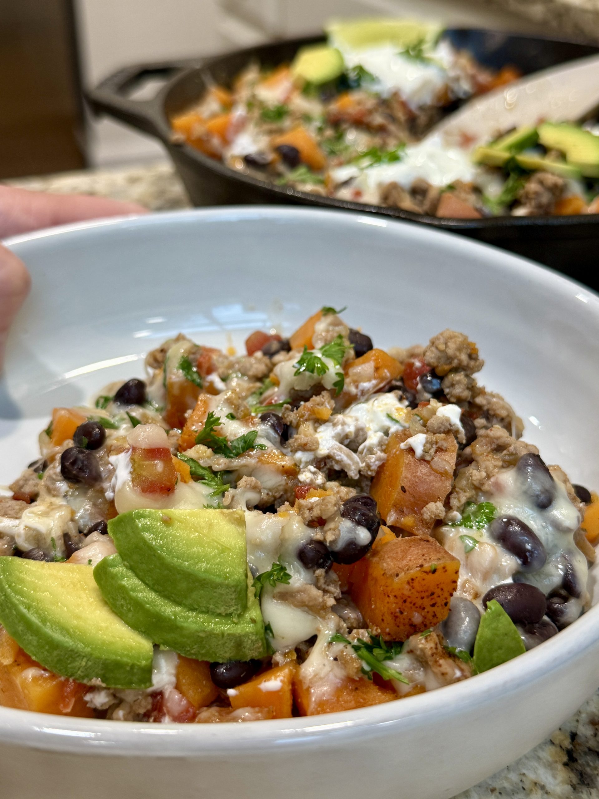 A bowl with sweet potatoes, ground turkey, beans, avocado slices, and sour cream 