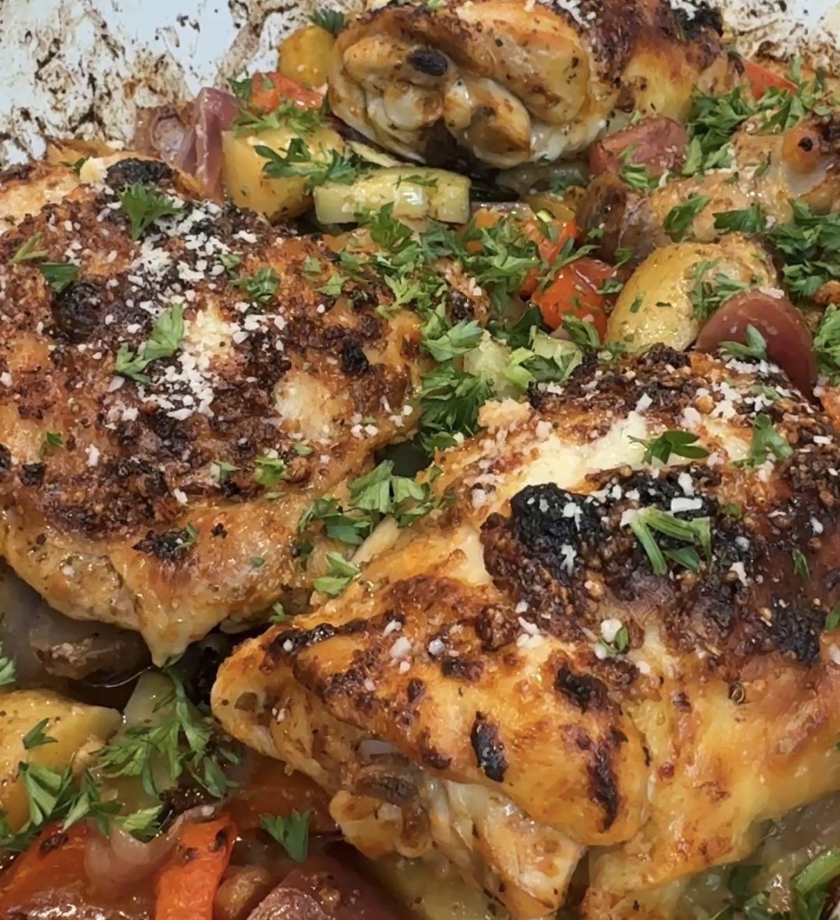 A baking dish with veggies and greek chicken thighs