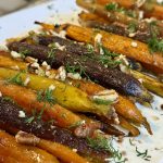 A platter with whipped feta and carrots, sprinkled with dill and pecans
