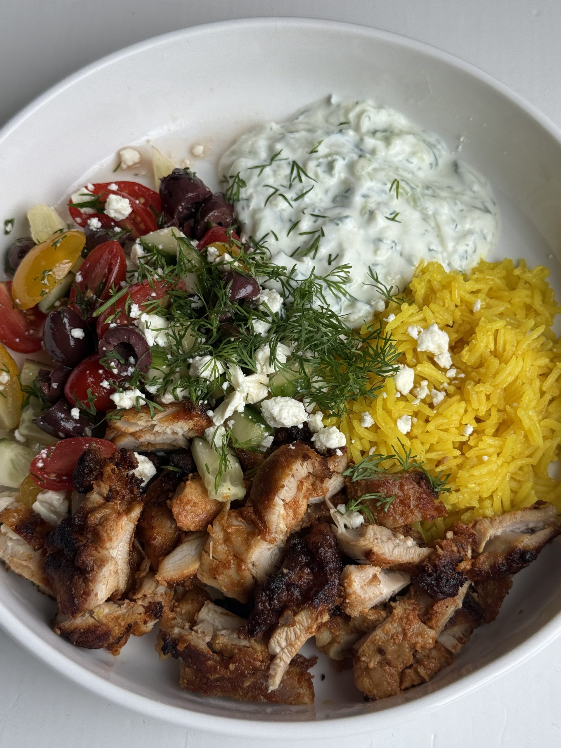 A bowl of chicken gyro meat, rice, tzatziki sauce, and Greek salad
