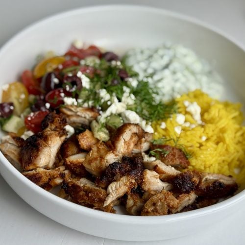 A bowl of chicken gyro meat, rice, tzatziki sauce, and Greek salad