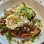 A roasted sweet potato half topped with spiced ground meat, dollops of cottage cheese, chopped pistachios, and fresh cilantro, served on a ceramic plate.