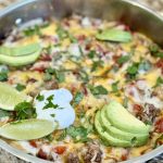 a skillet with cooked bell peppers, ground beef, cheese, avocado and sour cream