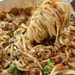 A close-up of noodles mixed with ground beef, broccoli, and shredded carrots in a pot, with a fork lifting a swirl of noodles above the mixture.