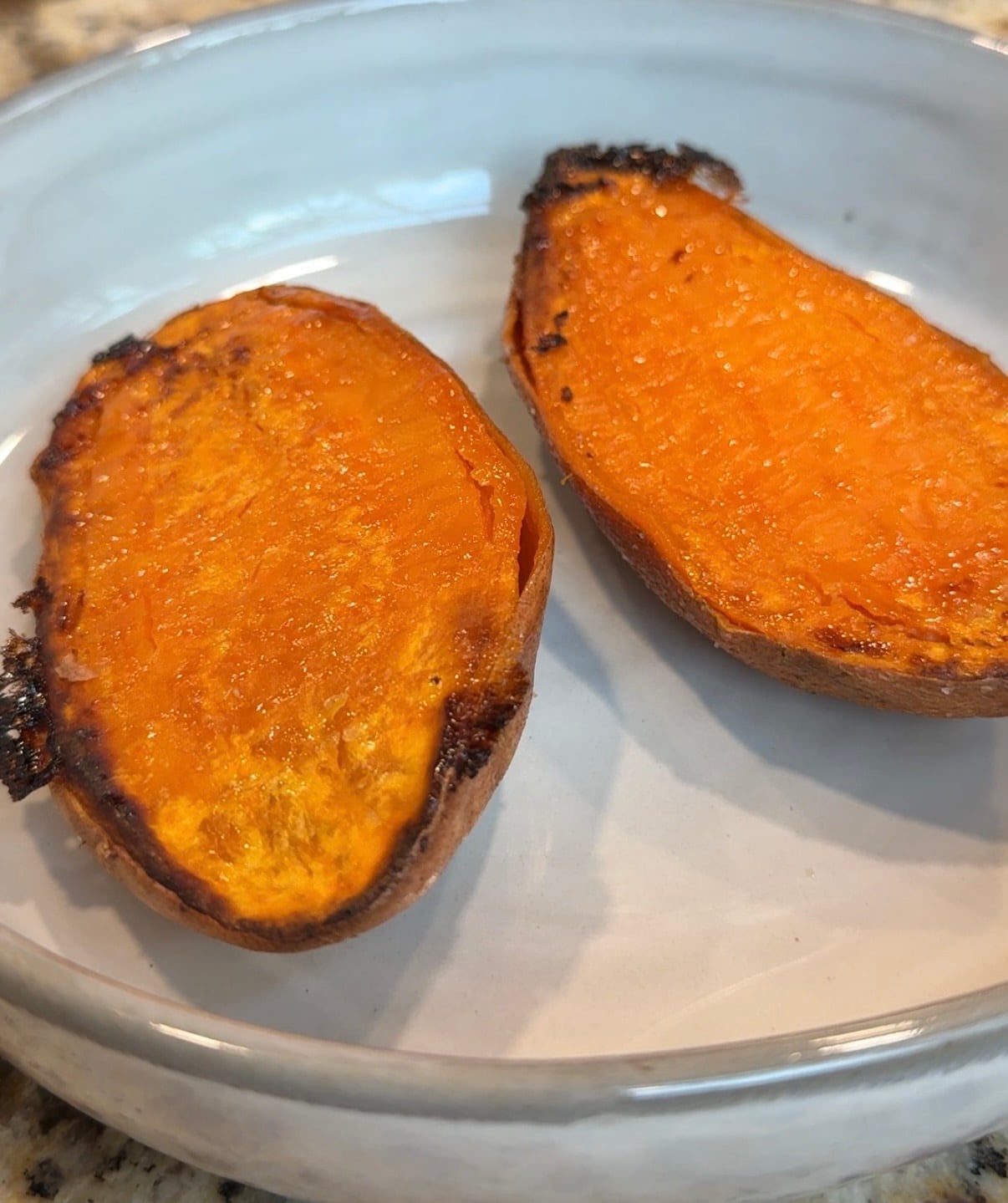 Two roasted sweet potato halves with caramelized edges sit on a light gray plate. The vibrant orange flesh appears soft and slightly glossy from roasting.