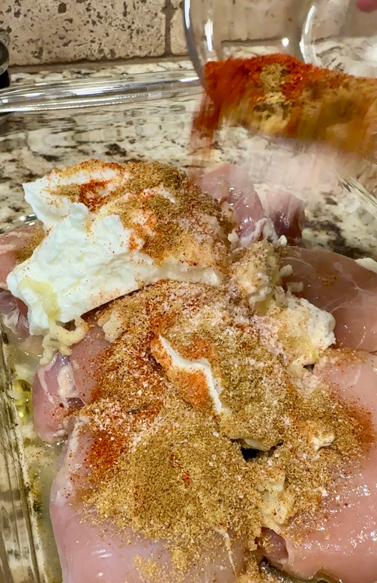 A glass container with raw chicken thighs and chicken gyro marinade on it