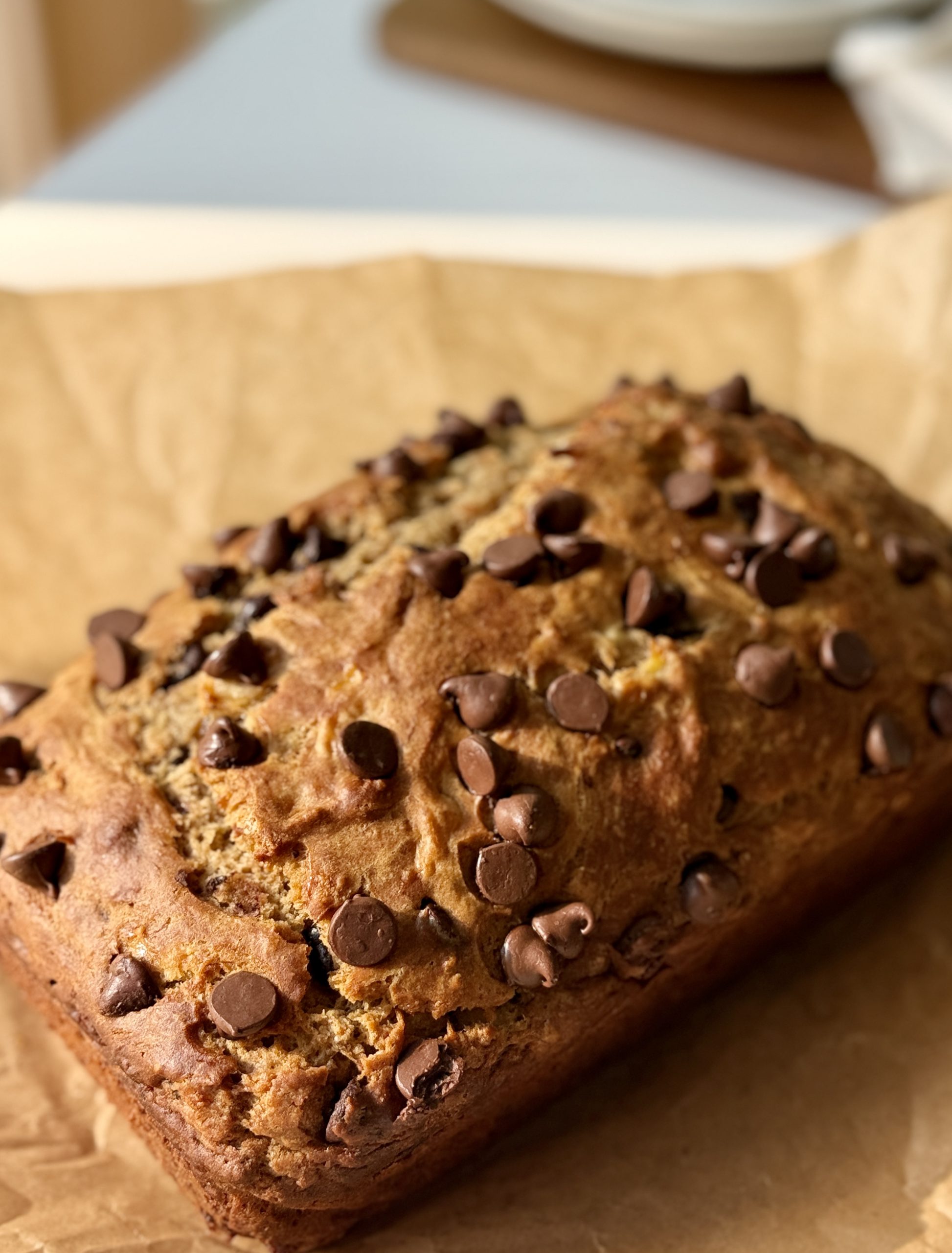 A freshly baked banana bread topped with melting chocolate chips sits on parchment paper.
