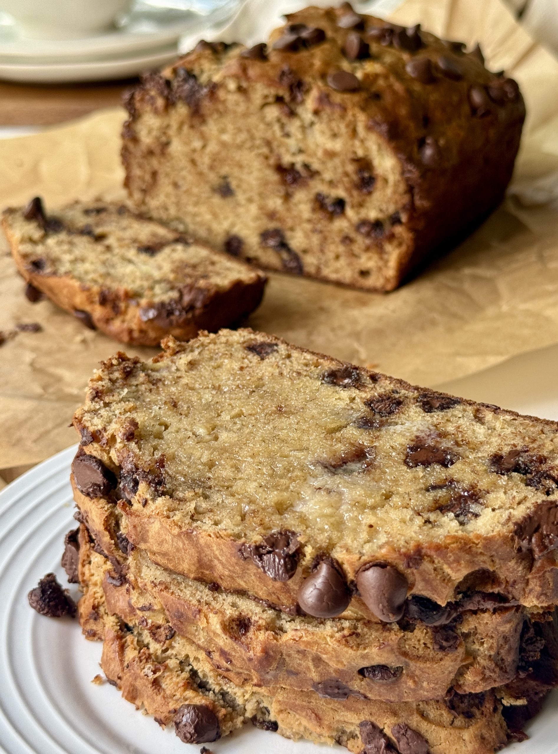 Close-up of sliced chocolate chip banana bread on a white plate. The bread is moist and studded with chocolate chips, creating a warm, inviting feel.