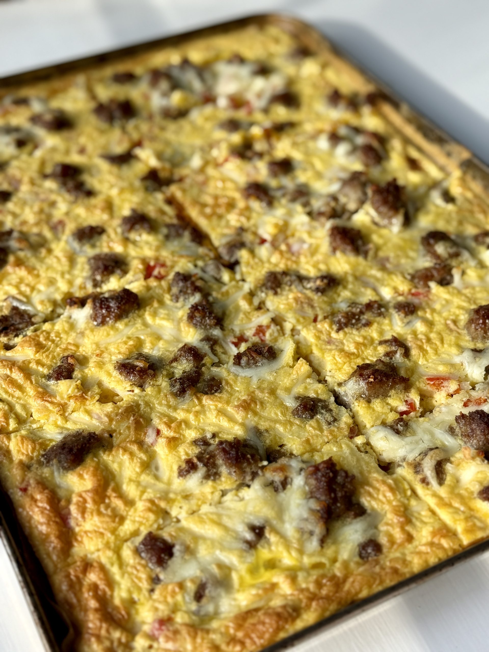 Golden baked breakfast casserole with scattered browned sausage pieces and melted cheese on a baking sheet. The surface is inviting and hearty.
