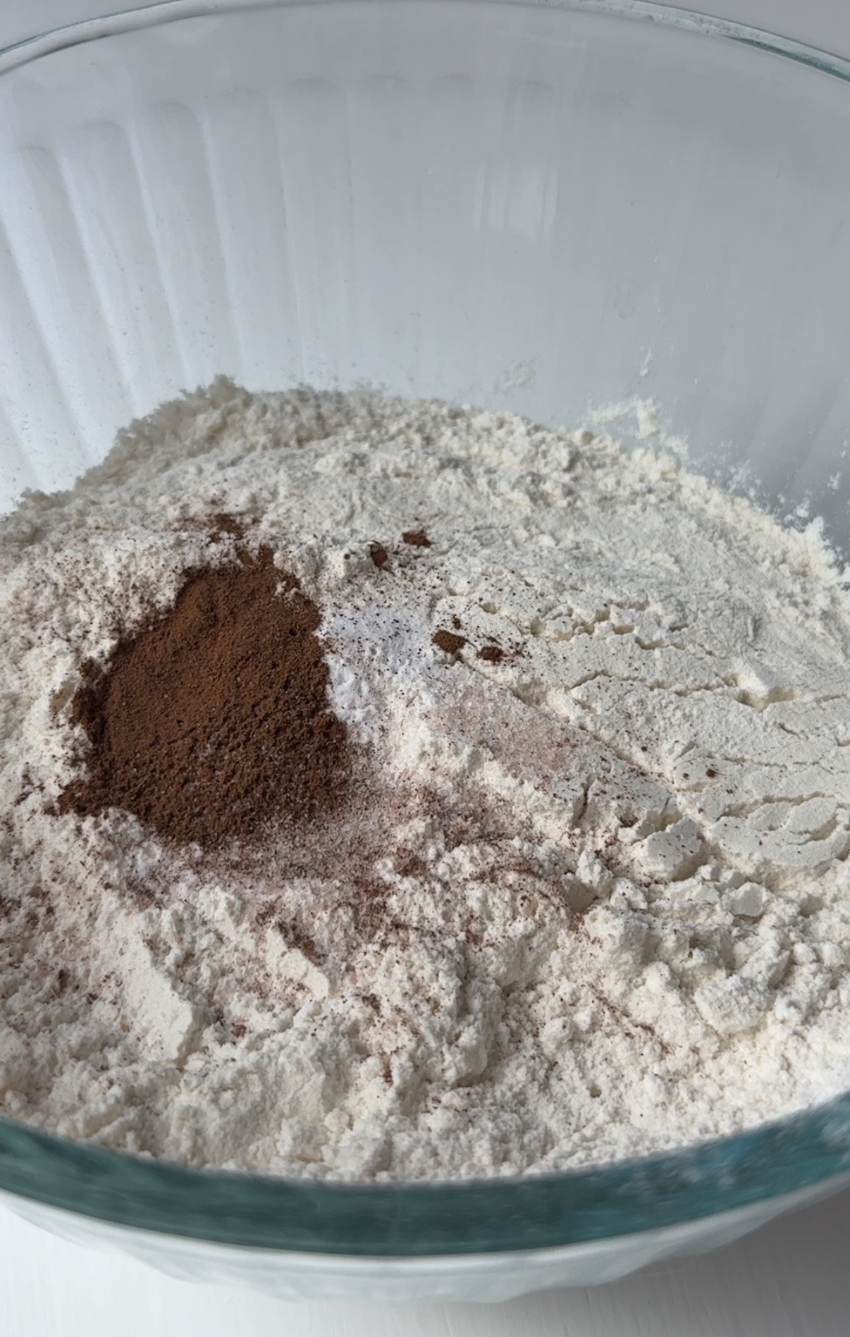 A clear glass bowl filled with flour and a small heap of cinnamon on top.