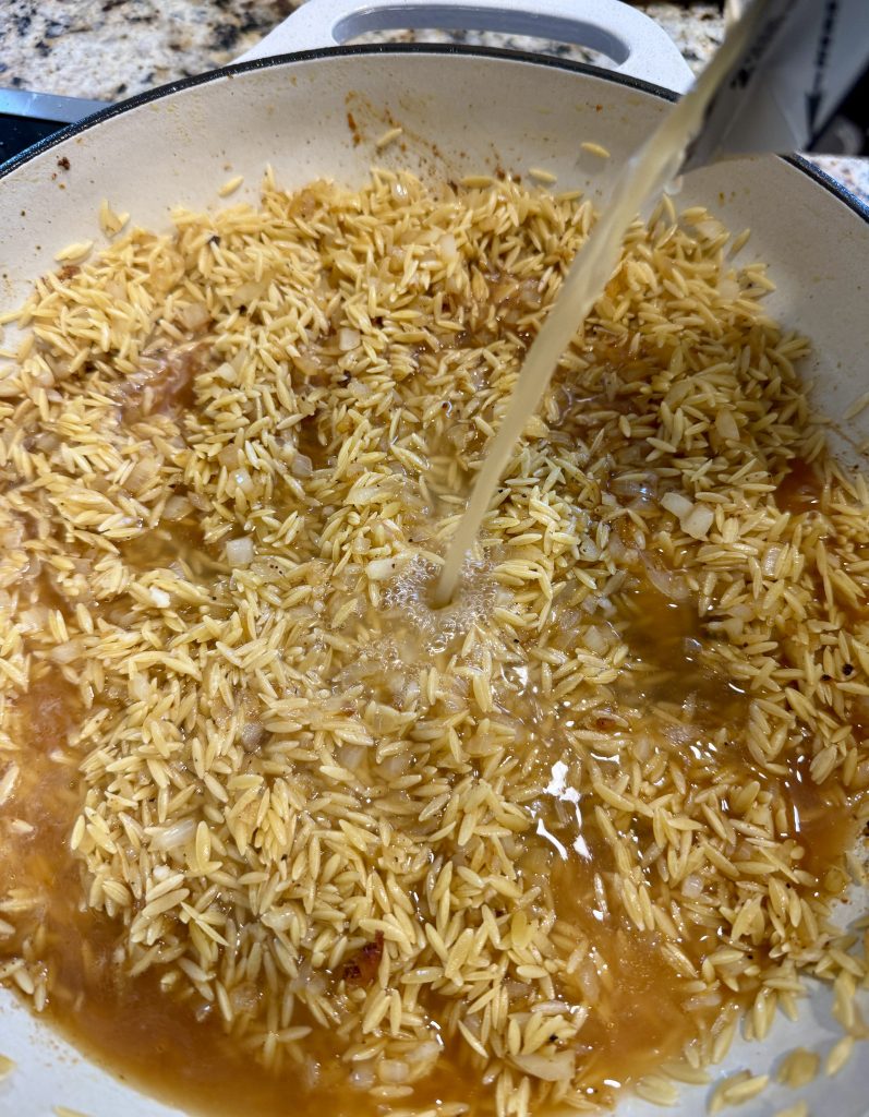 Adding the liquid to the pan of orzo. 