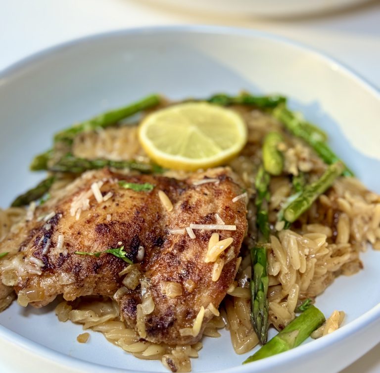 A plate of lemon chicken orzo garnished with a lemon slice.