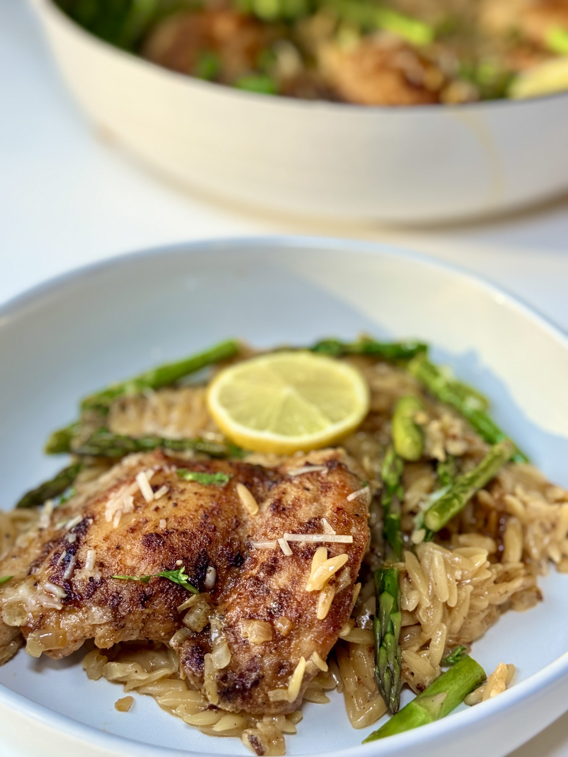 A plate of lemon chicken orzo garnished with a lemon slice.