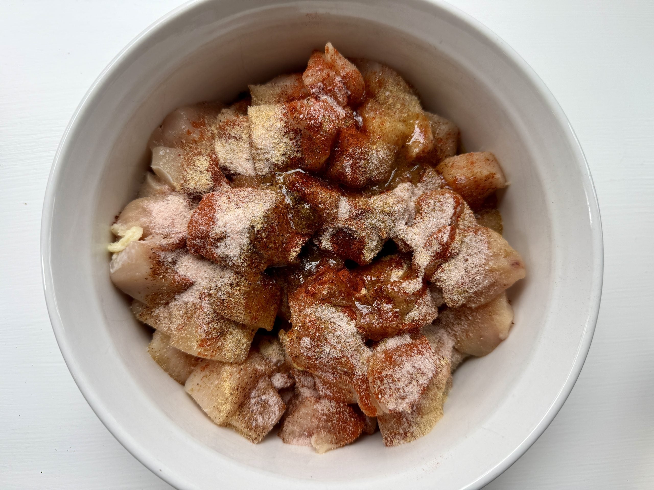 Cubed chicken pieces in a white bowl, coated with a mix of paprika and garlic powder, creating a seasoned, appetizing appearance against a clean background.