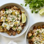 Two bowls filled with roasted potatoes, grilled chicken, and corn topped with creamy sauce and crumbled cheese. Garnished with lime and cilantro.