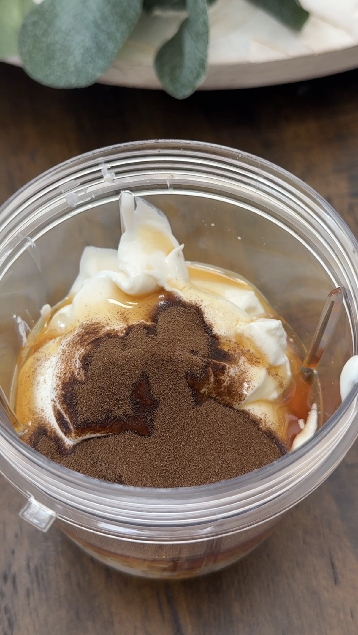 A plastic blender cup containing dollops of yogurt, a drizzle of honey, and a heap of vanilla on top, ready to be blended.