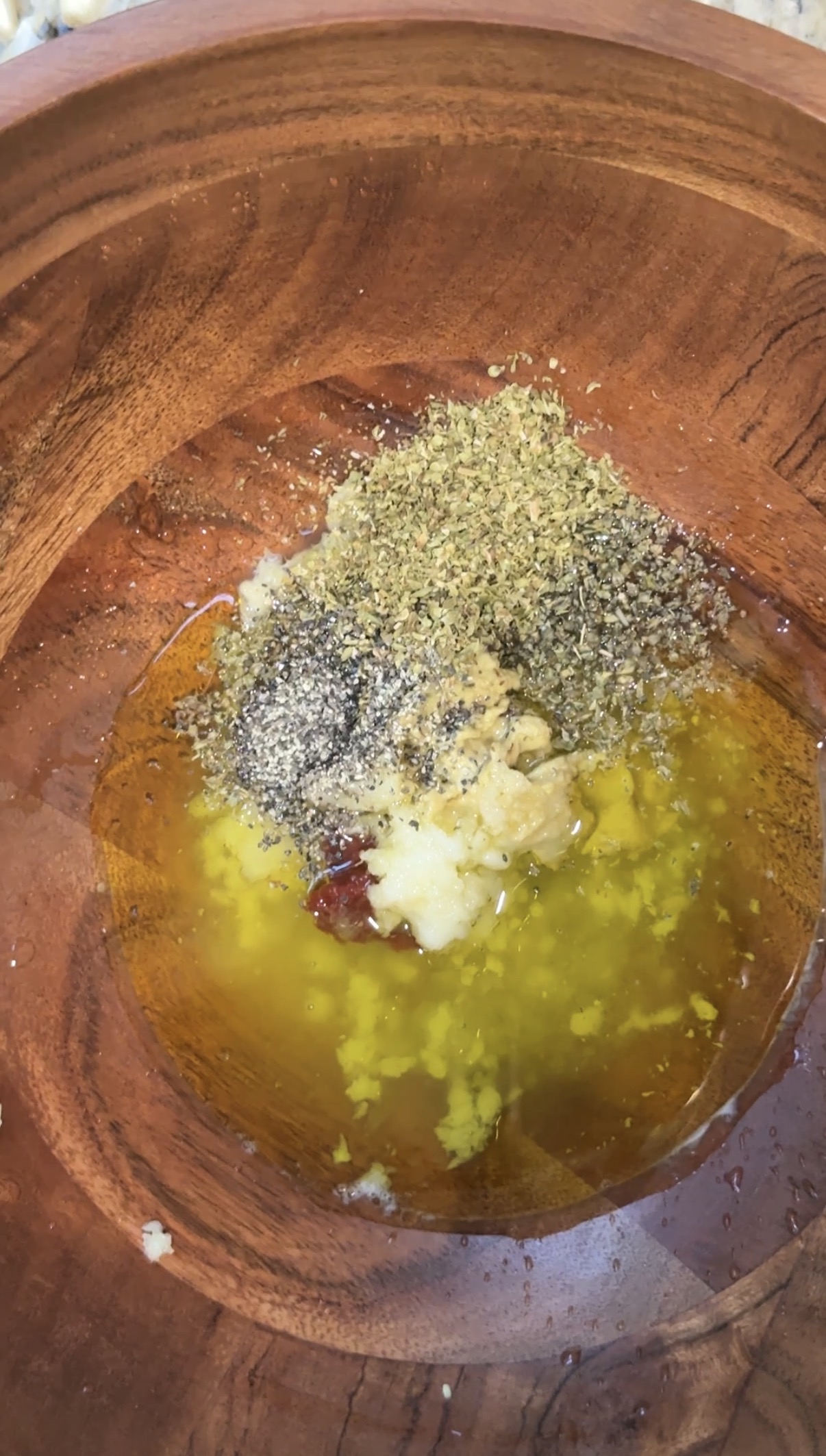 Wooden bowl with marinade ingredients: lemon, olive oil, tomato paste, and seasonings.