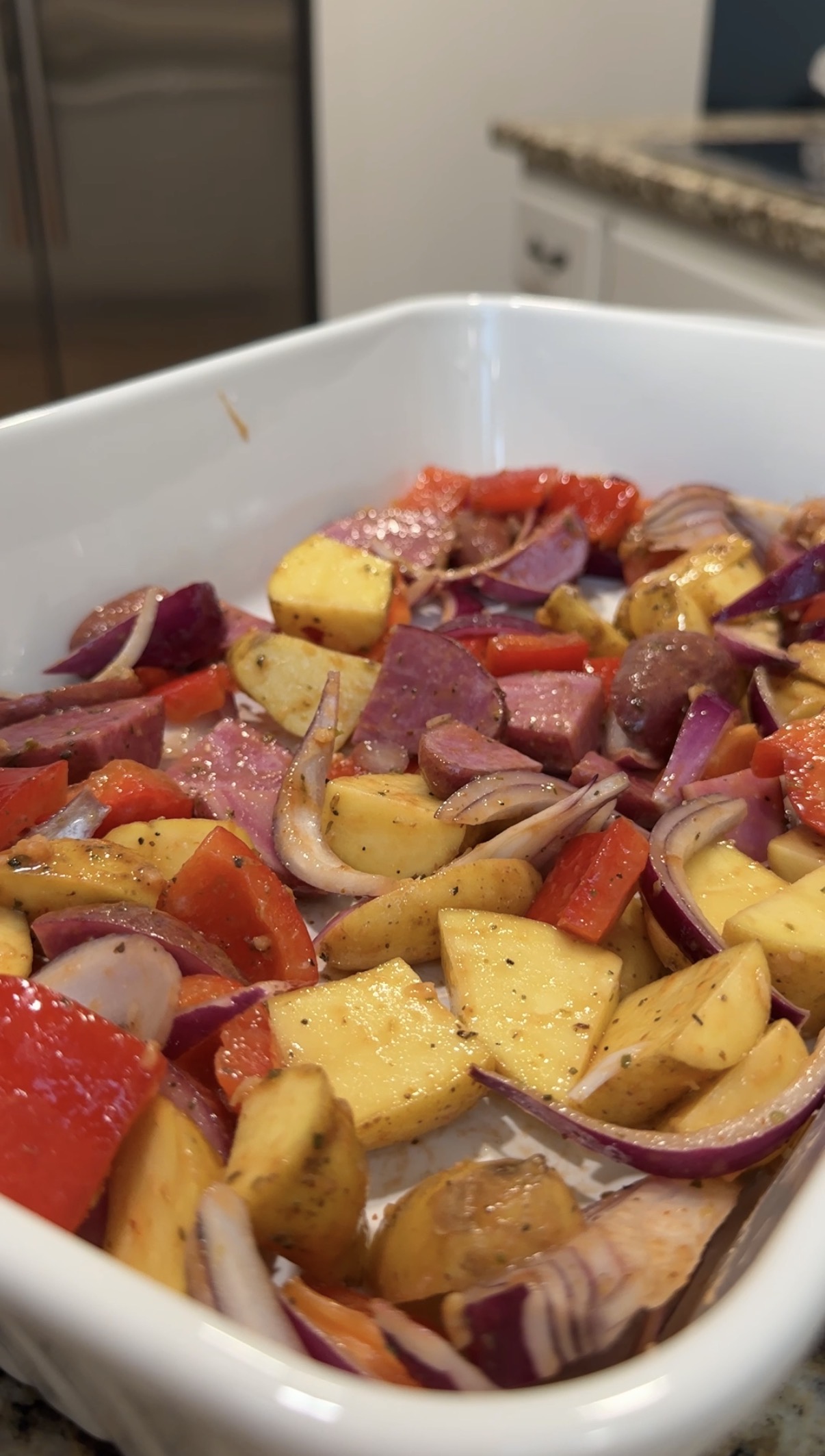 Baking dish with chopped up potatoes, red onions, zucchini, and red bell peppers.