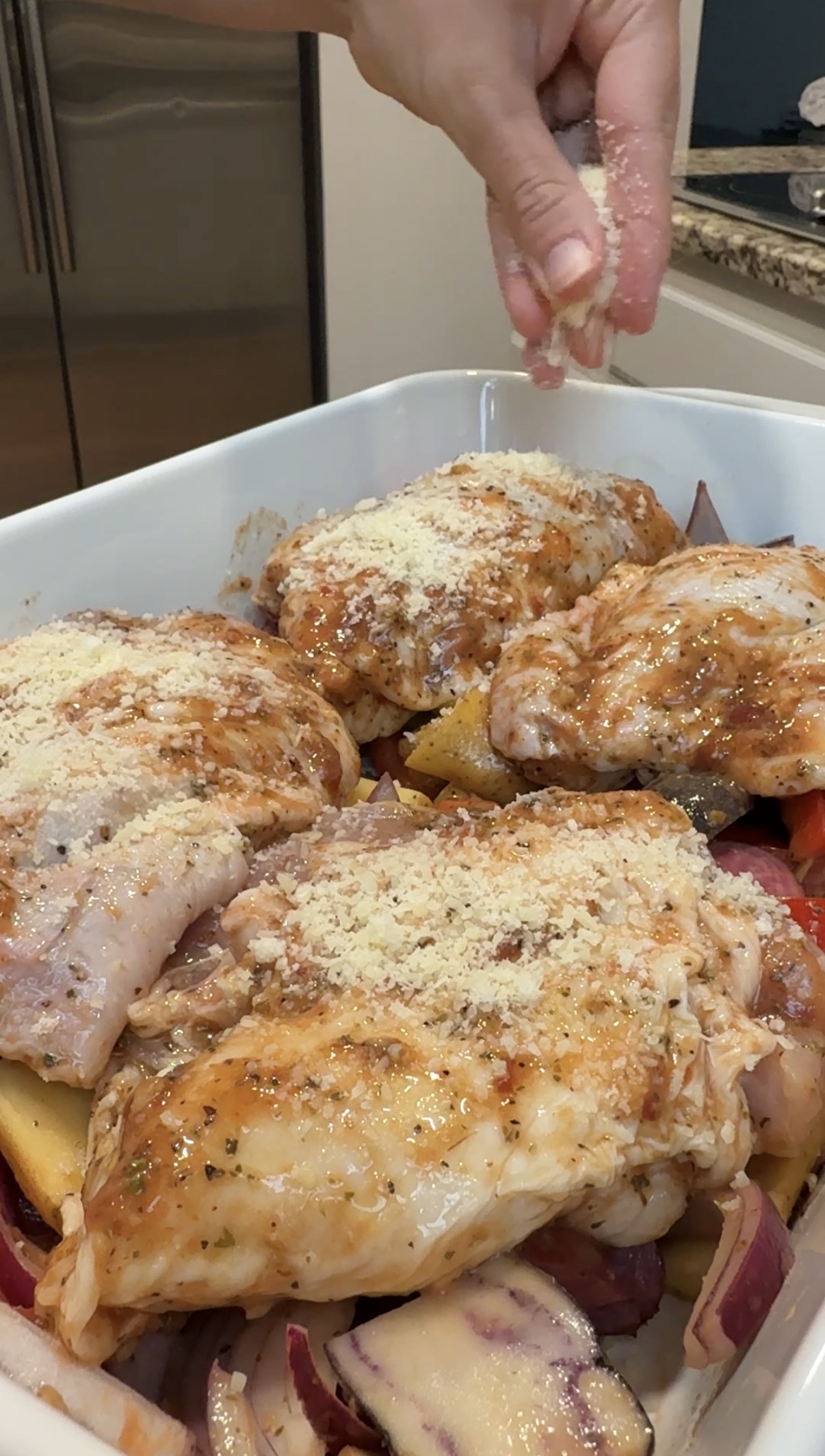 Baking dish with veggies and marinated chicken thighs, sprinkled with parmesan cheese