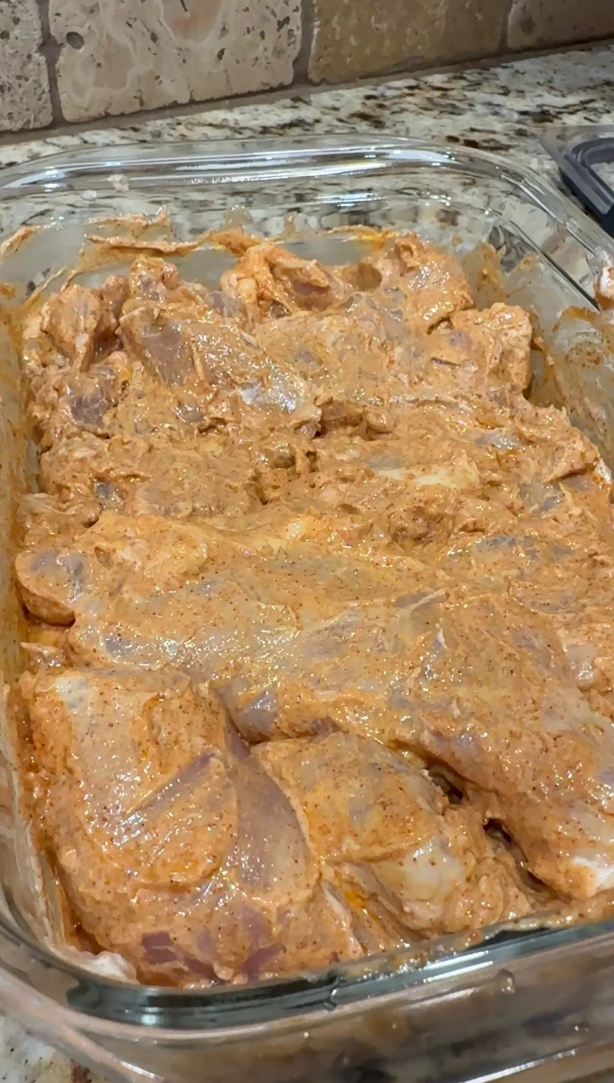A glass container with raw chicken thighs and chicken gyro marinade on it