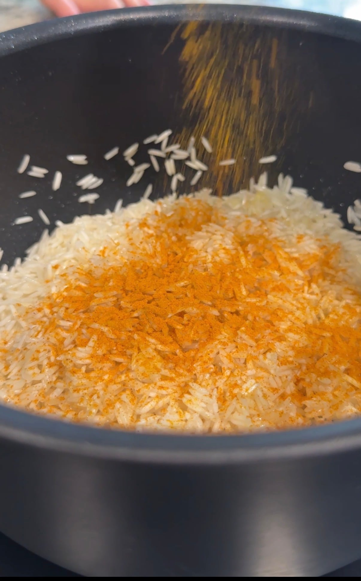 A cooking pot with rice and turmeric seasoning being sprinkled on it