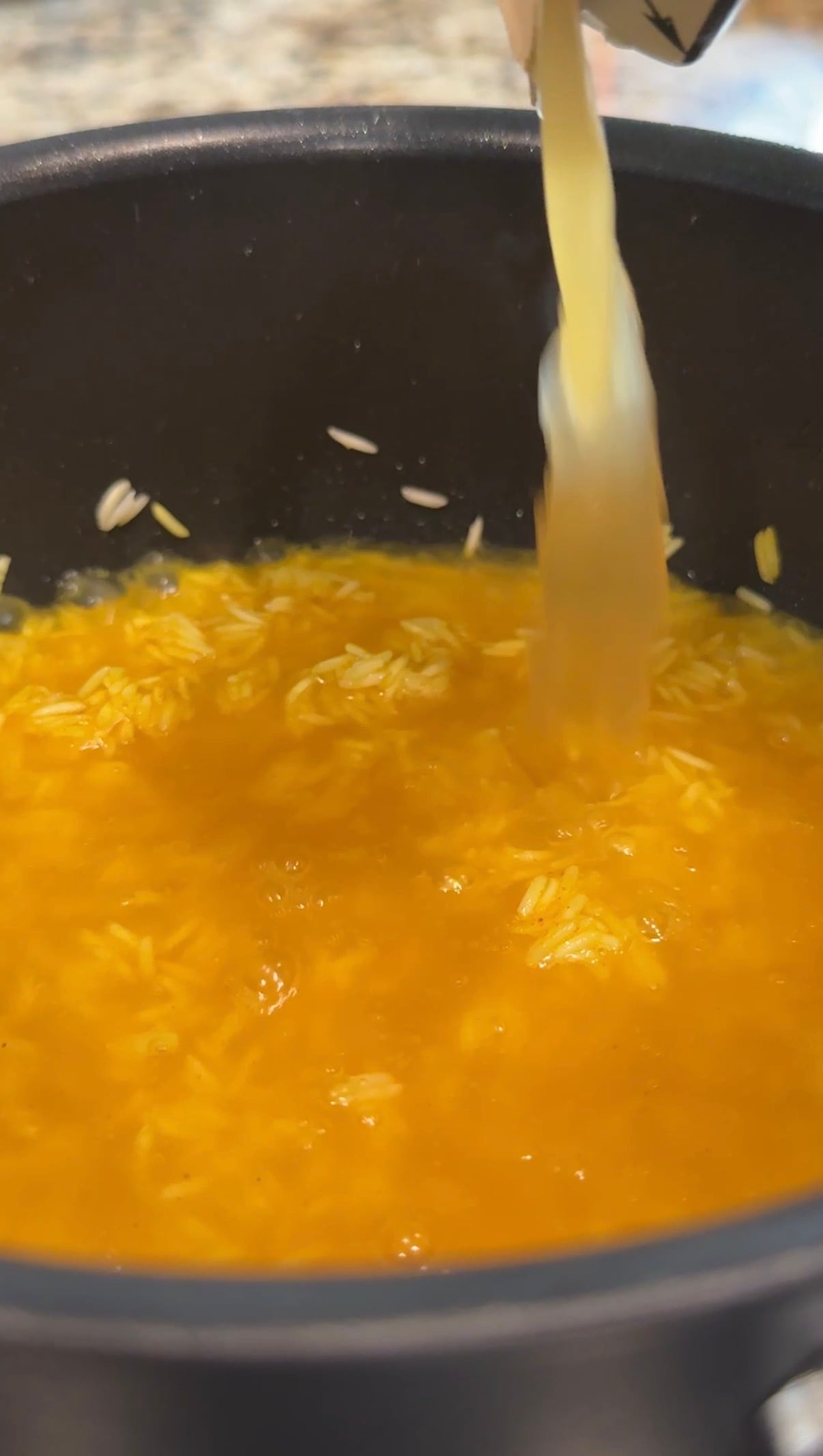 A cooking pot with turmeric lemon rice and bone broth being poured into it