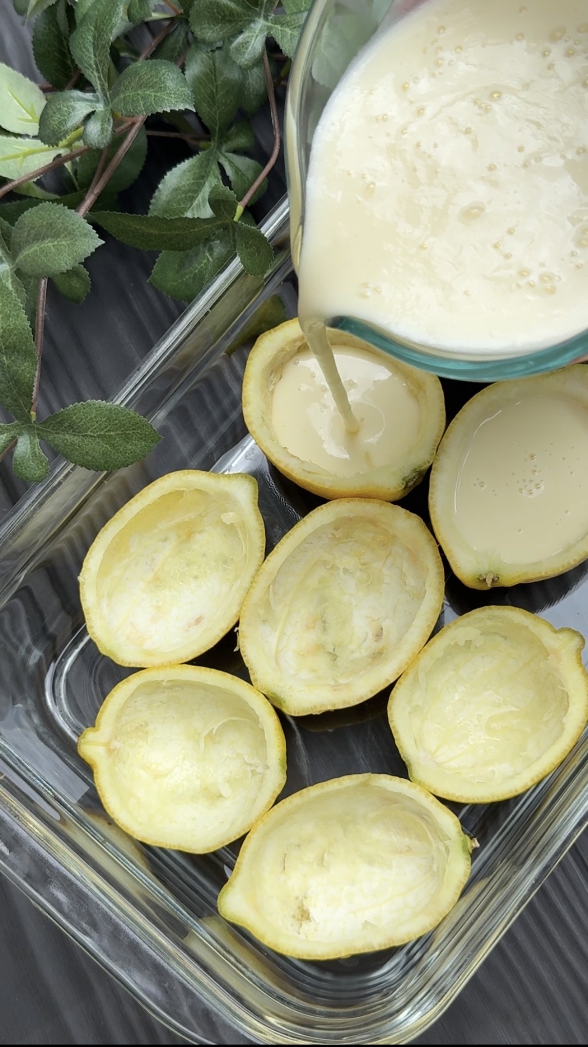 Halved and peeled lemons arranged in a glass dish and a measuring cup with the cream lemon mixture being poured into the lemon skins.