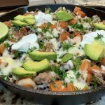 A skillet with sweet potatoes, ground turkey, beans, avocado slices and sour cream