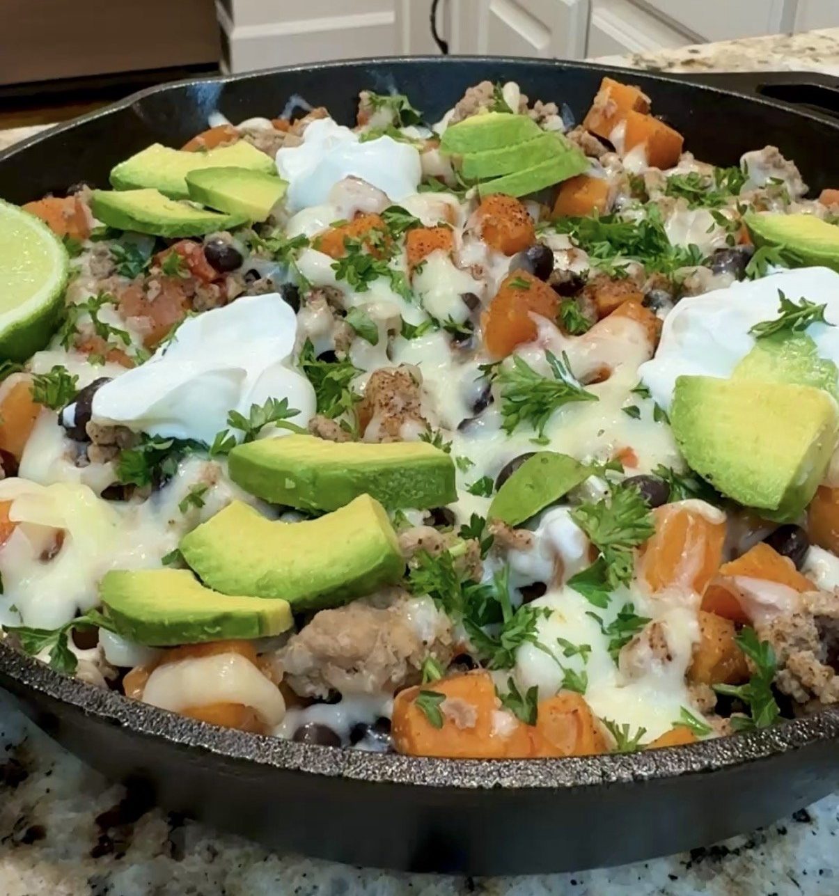 A skillet with sweet potatoes, ground turkey, beans, avocado slices and sour cream