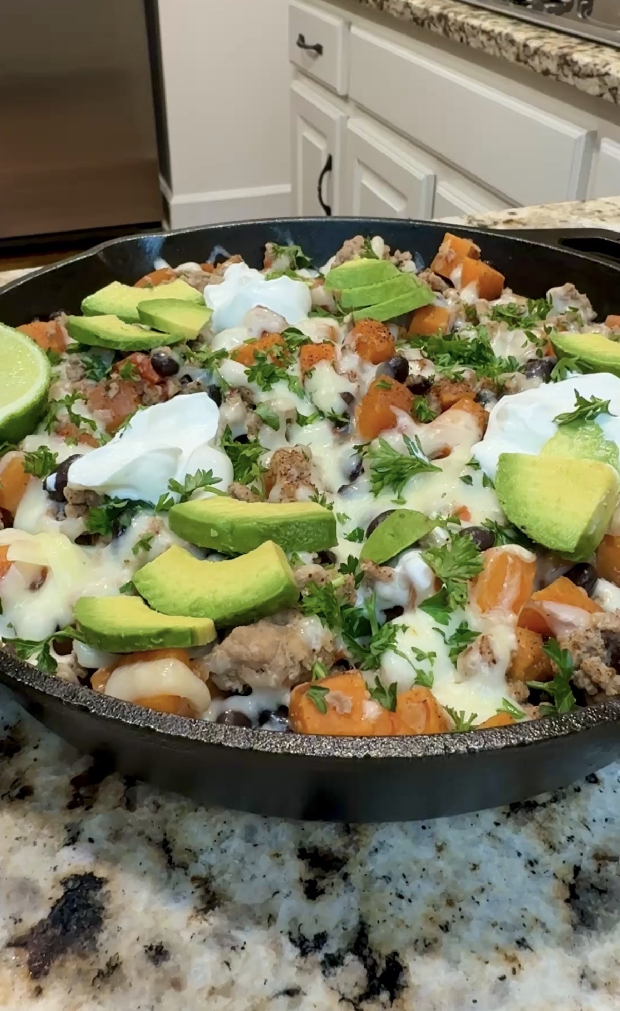 A skillet with sweet potatoes, ground turkey, beans, avocado slices and sour cream