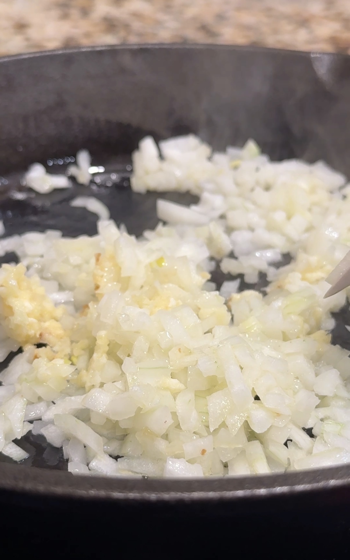 A skillet with diced onions and minced garlic that are getting sauteed