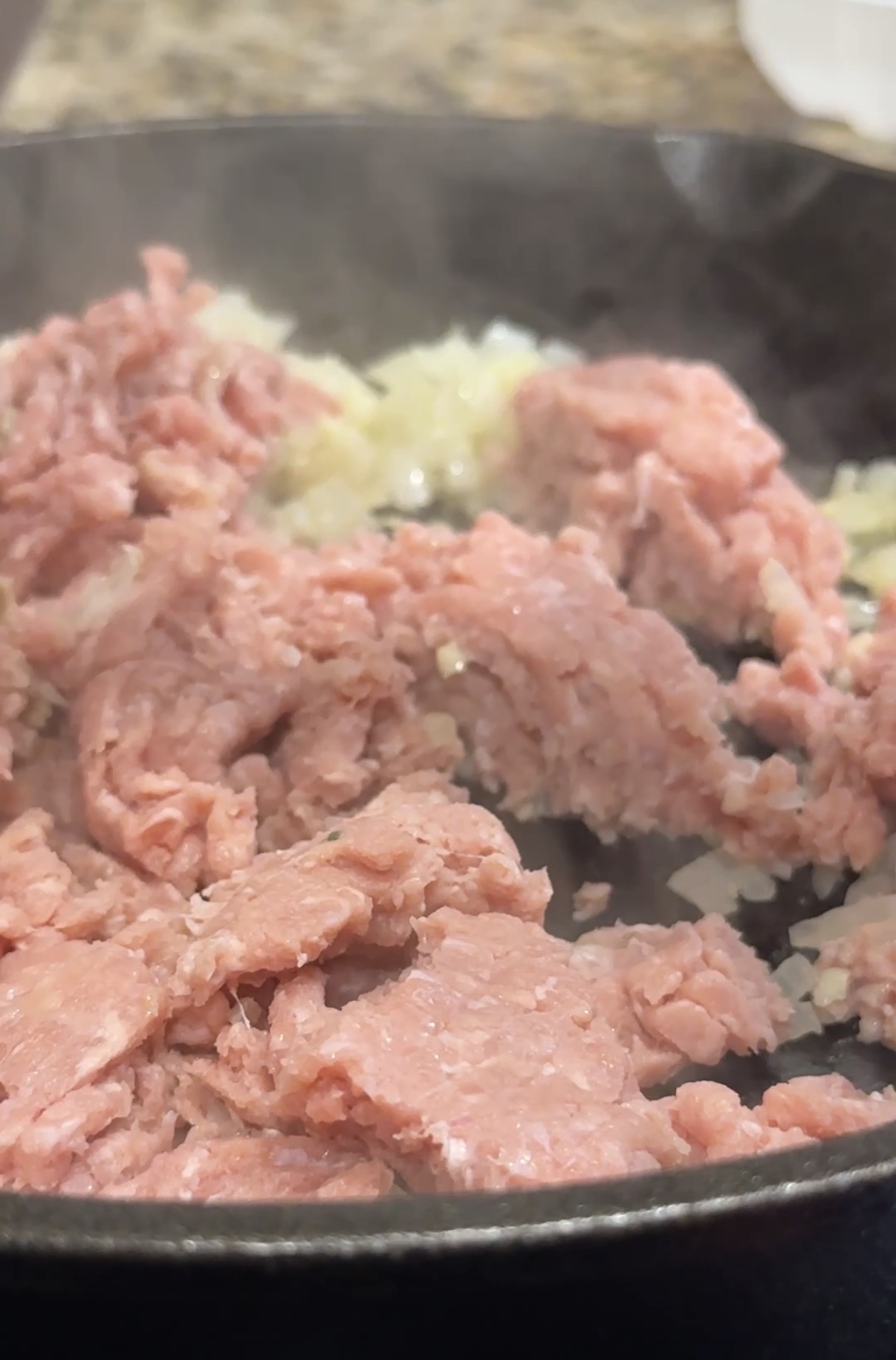 A skillet with diced onions, minced garlic and ground turkey that are getting sauteed