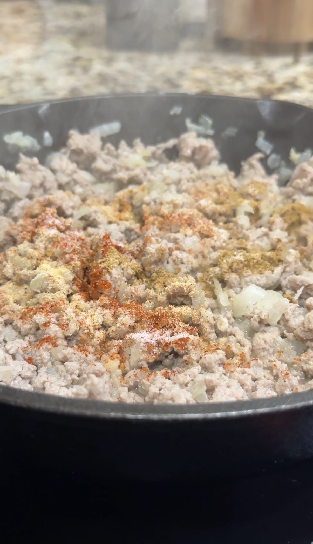A skillet with ground turkey, diced onions. minced garlic that are getting sauteed and are sprinkled with seasonings.