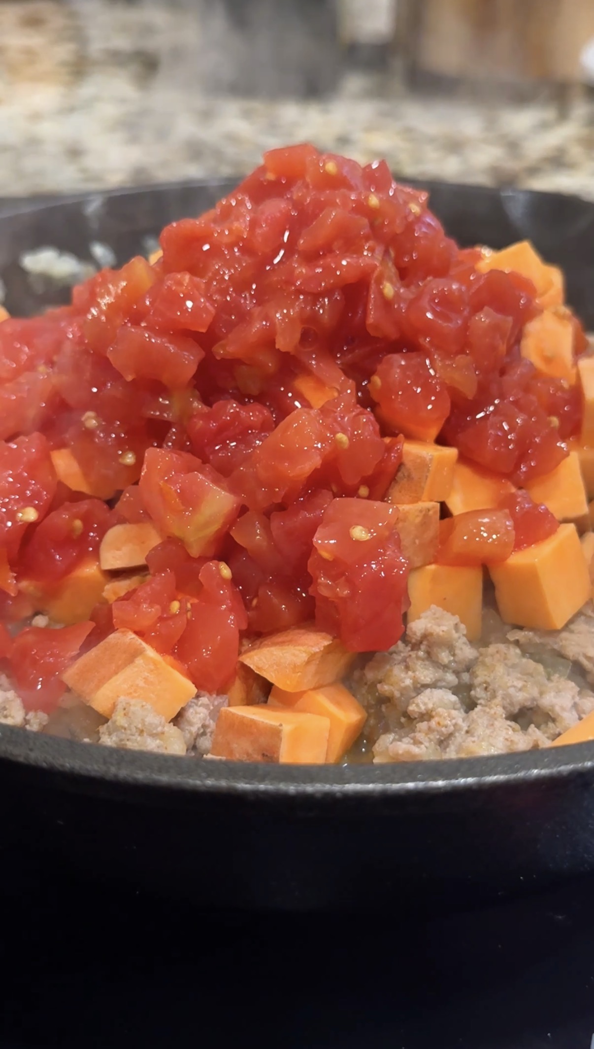 A skillet with cooked ground turkey and diced sweet potatoes and diced canned tomatoes