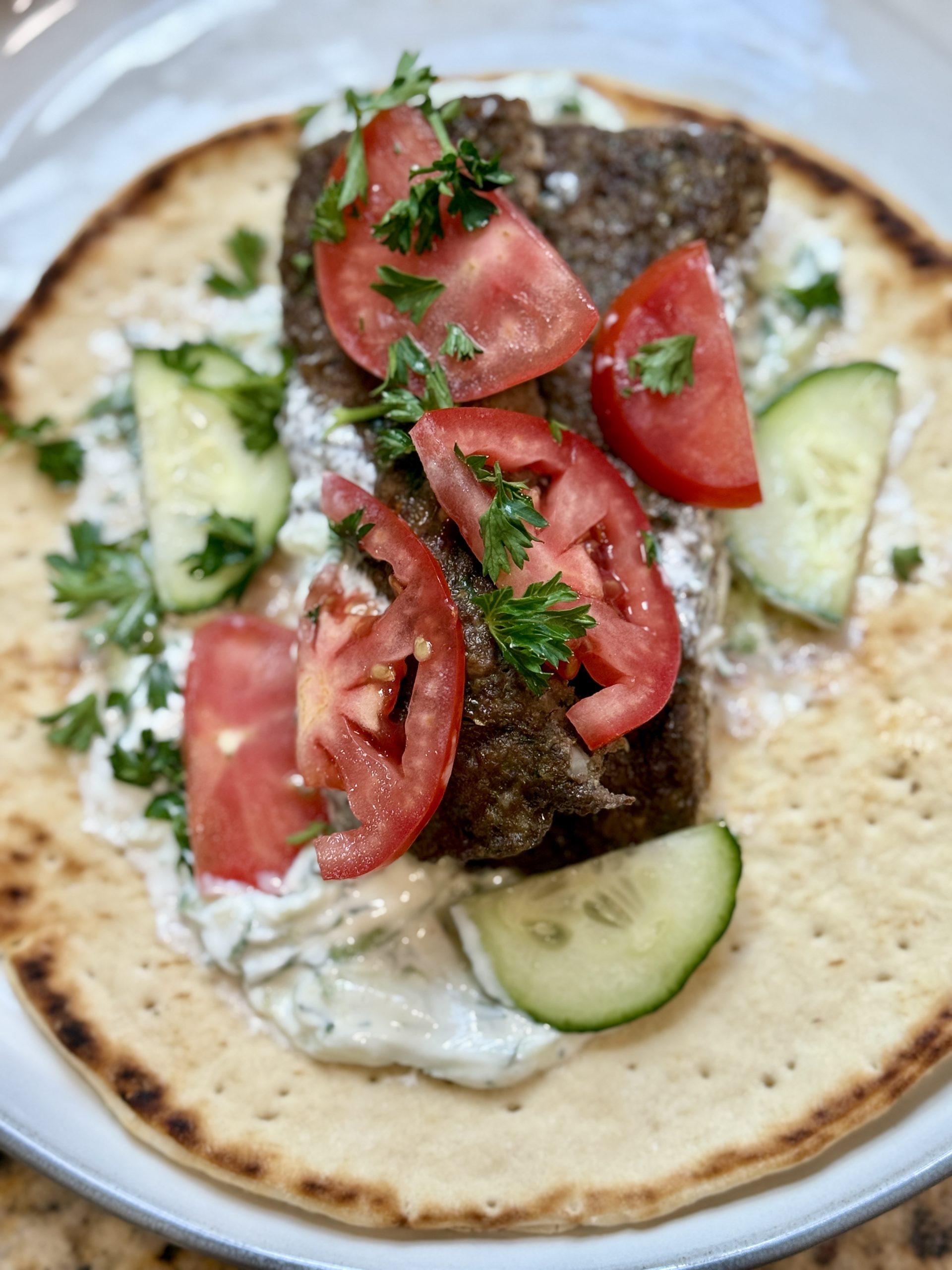 a plate with pita bread, tzatziki sauce and juicy oven-baked beef kebabs, topped with cucumber and tomatoes