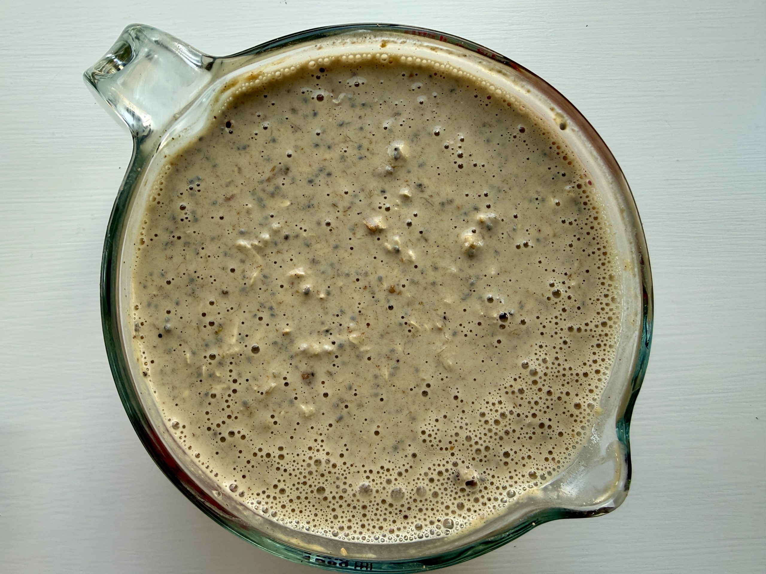 A glass measuring cup filled with a thick, bubbly brown mixture, sits on a white surface.
