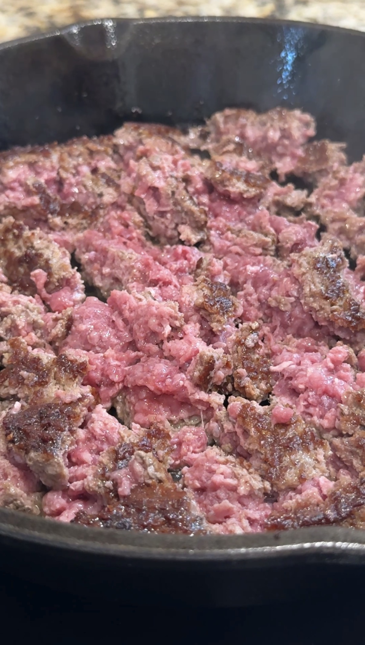 Ground beef cooking in a pan, with some parts browned and other areas still pink and raw.