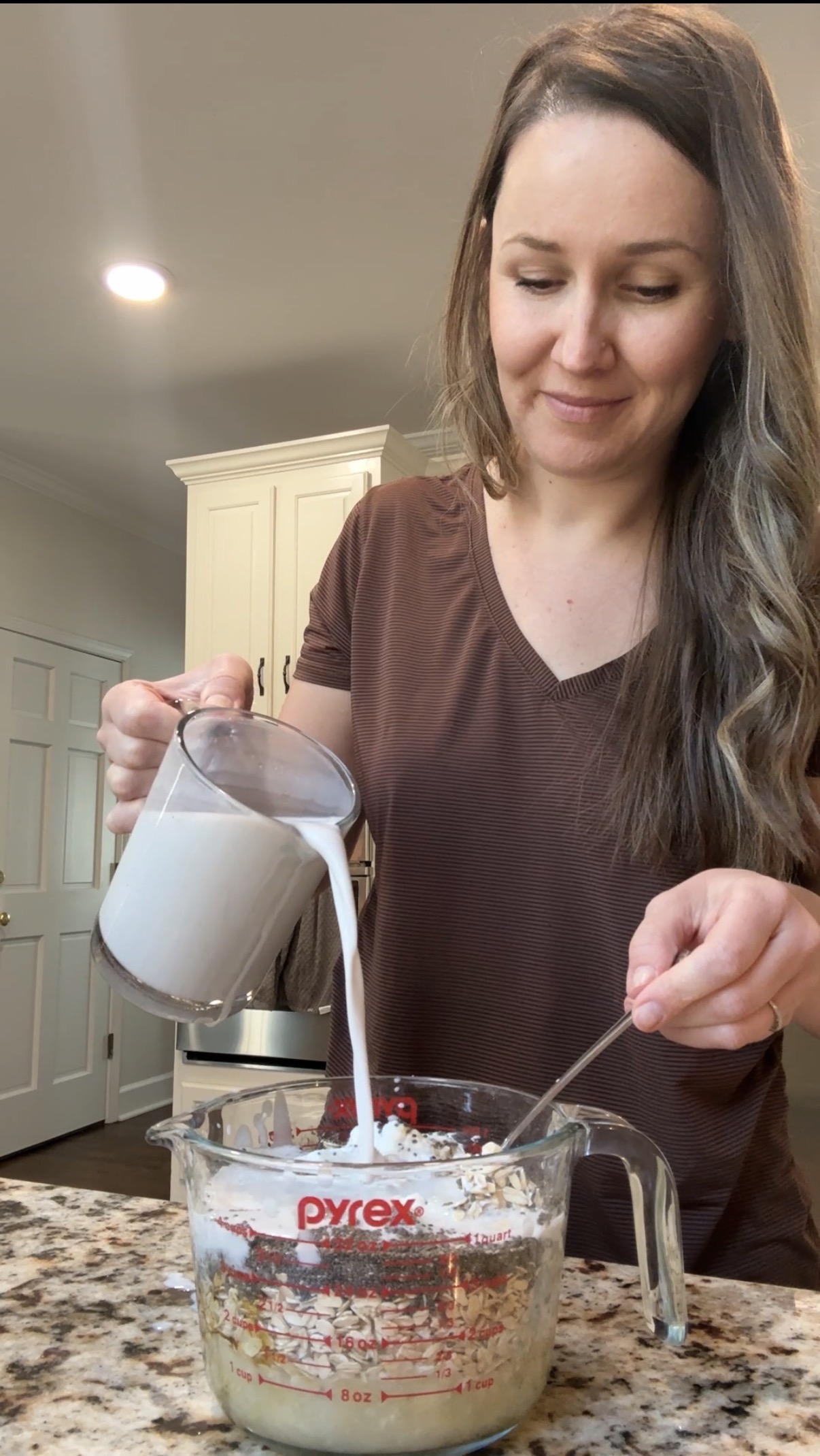 A person pouring milk into a glass jar, filled with the banana peanut butter overnight oats ingredients in it