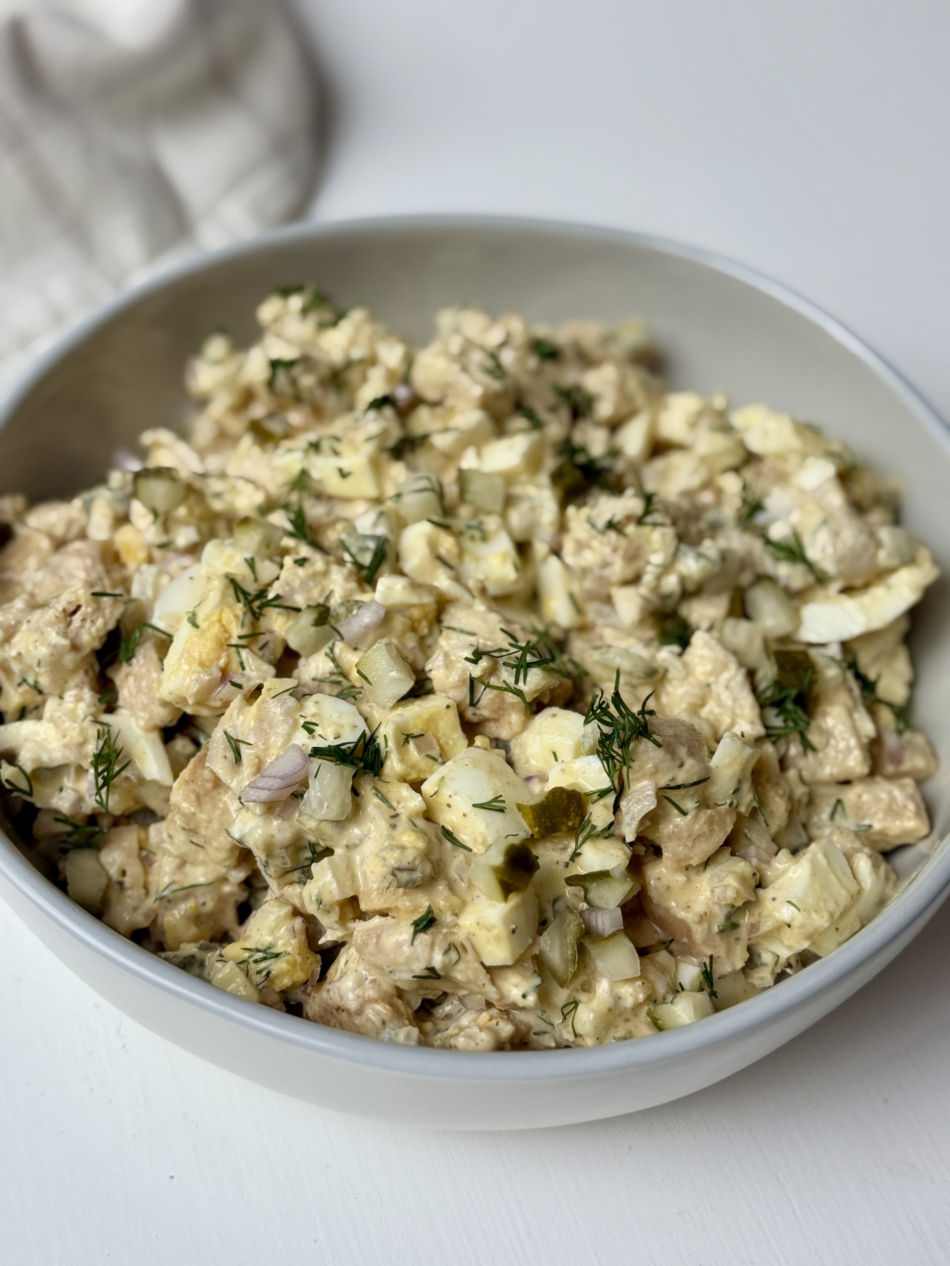 A bowl filled with a chicken salad mixed with eggs, dill, pickles, shallots, yogurt, mayo, and dijon mustard. 