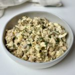 A bowl filled with a chicken salad mixed with eggs, dill, pickles, shallots, yogurt, mayo, and dijon mustard.