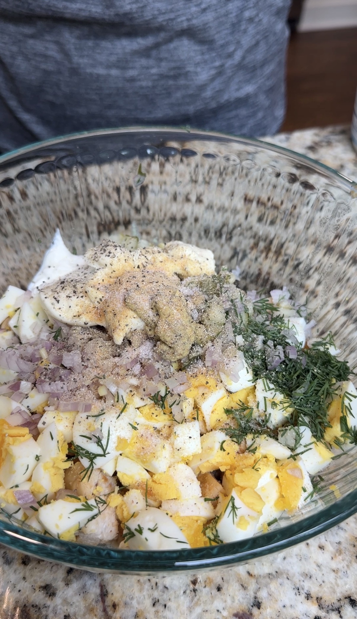 A bowl filled with a chicken salad ingredients, which are eggs, dill, pickles, shallots, yogurt, mayo, and dijon mustard.