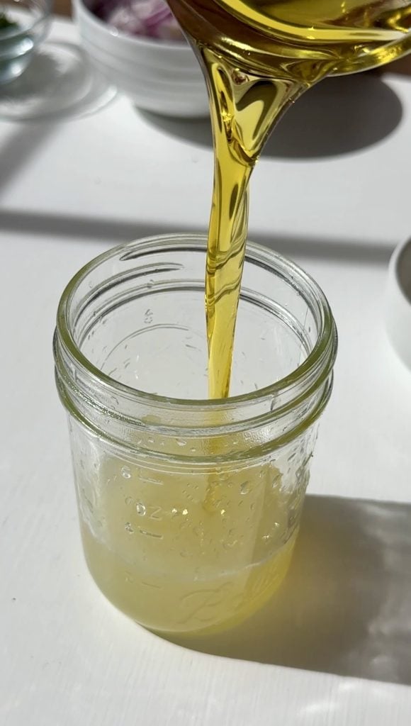 Golden liquid, likely oil, being poured into a glass jar already containing a light yellow liquid.