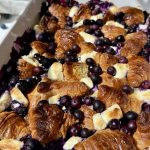 Blueberry lemon croissant bake topped with fresh blueberries and powdered sugar in a white baking dish